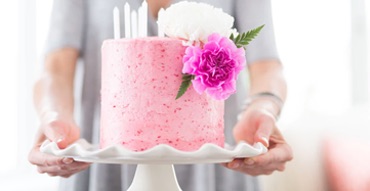 A woman holding a flower decorated cake on a display tray.