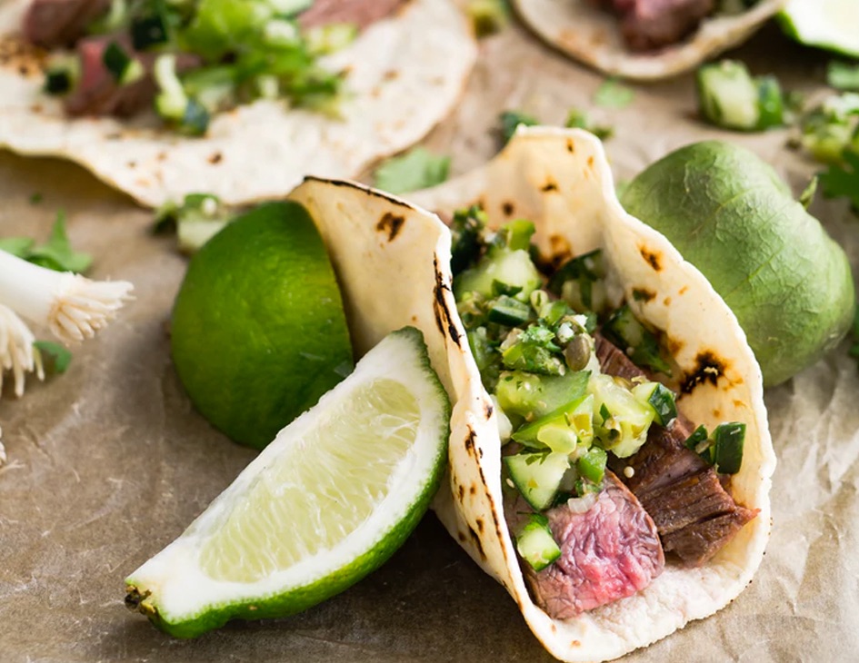 Close up shot of a spicy beef wrap surrounded by limes and spices.